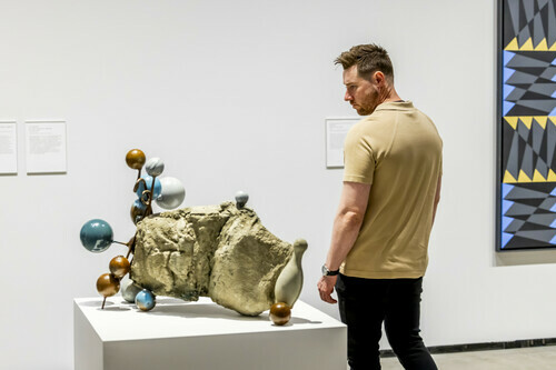 A man looks at a sculpture with circular bulbs protruding from it.