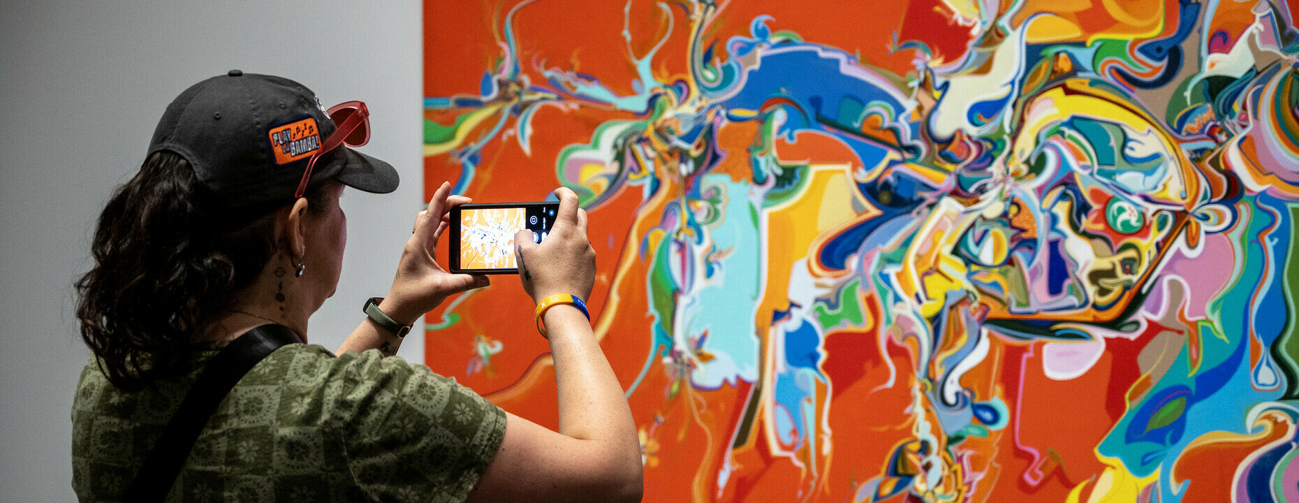 A woman takes a picture of a bright red canvas splattered with multicoloured paint.