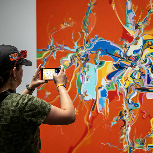 A woman takes a picture of a bright red canvas splattered with multicoloured paint.