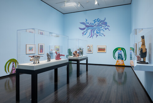 An elderly woman smiles at a multicoloured sculpture in the gallery.