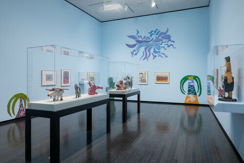 An elderly woman smiles at a multicoloured sculpture in the gallery.