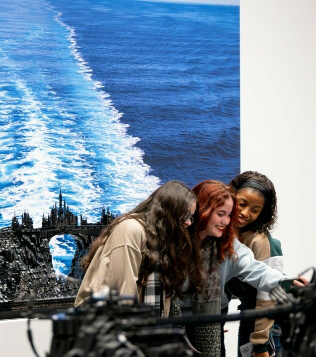 Three people post for a selfie in front of a sculpture and decal in Ekow Nimako: Building Black Civilizations - Journey of 2,000 Ships.