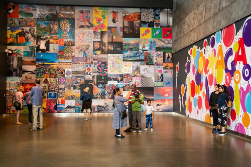 A group of people explore a wall filled with multicoloured art created by the community.