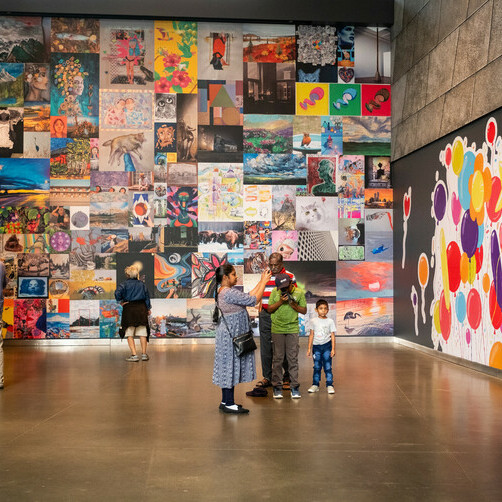 A group of people explore a wall filled with multicoloured art created by the community.